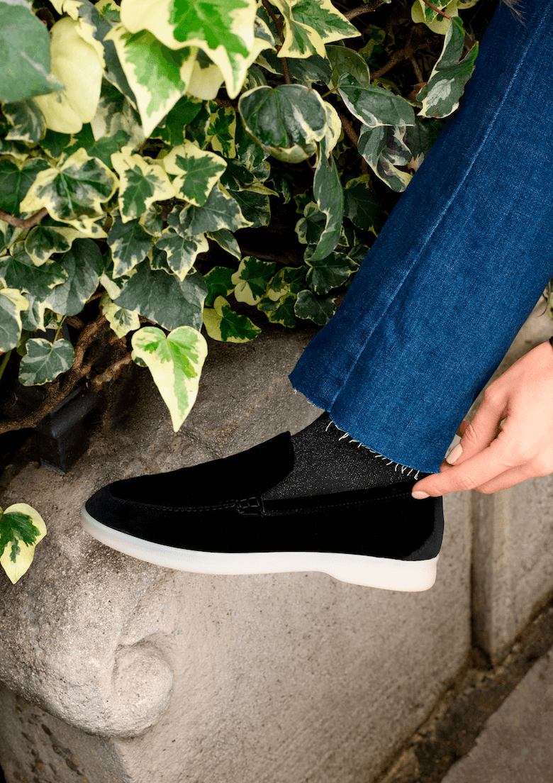 Mocassini Vegani in Velluto Nero indossati con jeans, posizionati accanto a piante verdi.