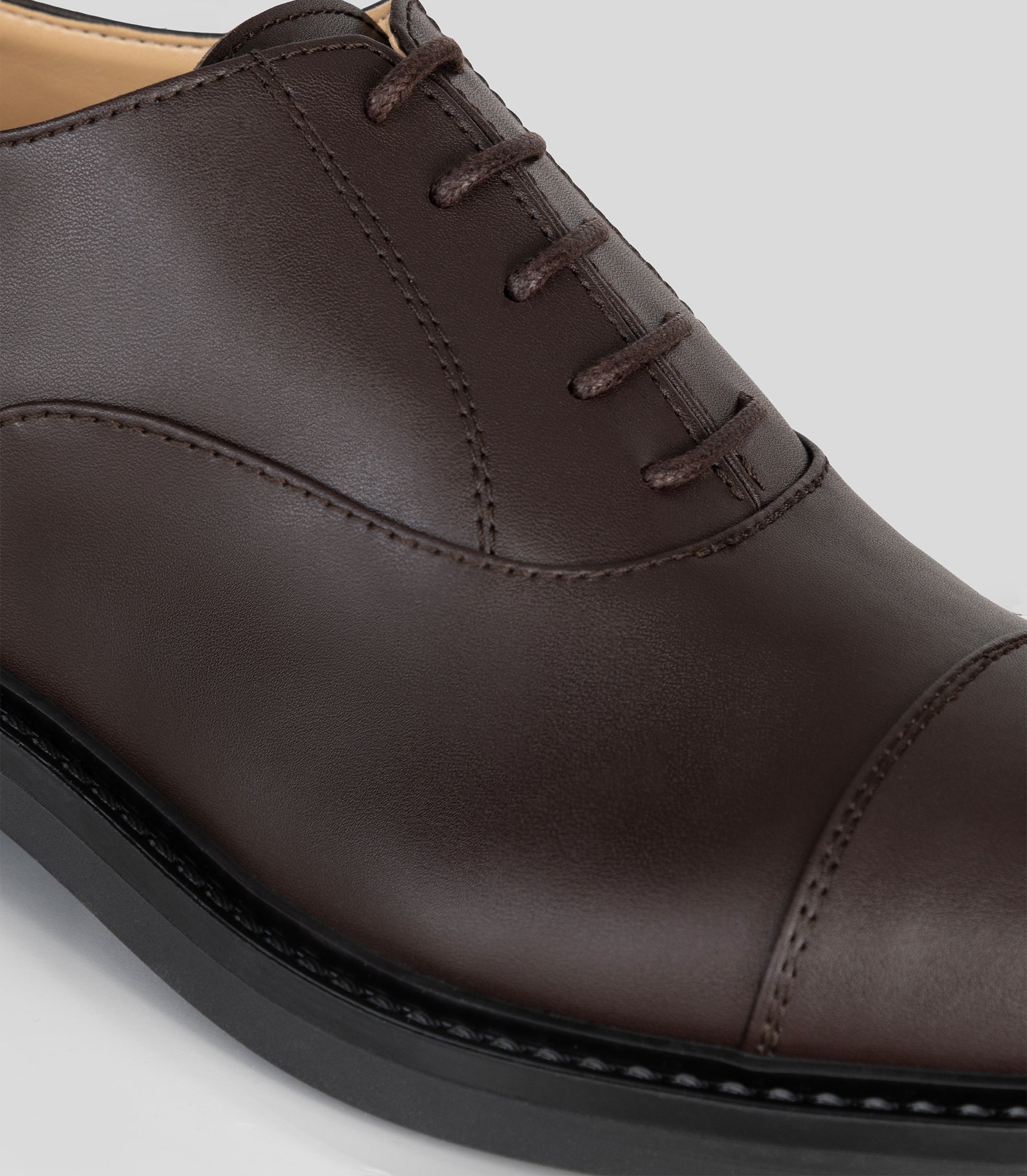 Vegan Oxford - Woman close-up of lace-up brown shoe showcasing Blake Construction details.