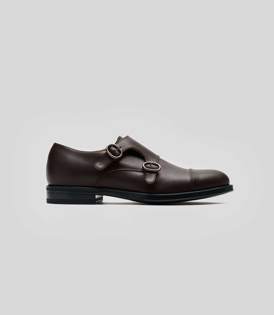 Vegan Monk Strap - Man showing a stylish brown monk strap shoe with double buckles on a grey background.